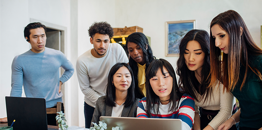 A publishing team gathered around a laptop, reviewing work together.